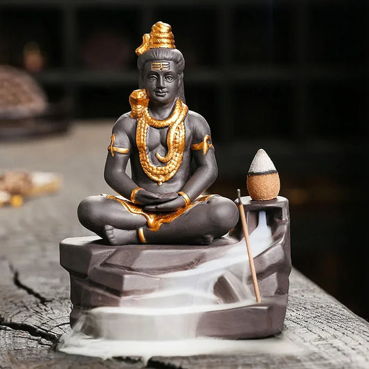 Incensário cascata com imagem de Shiva em resina, disponível em duas versões: mão erguida (proteção) ou mãos baixas (tranquilidade), com fumaça em cascata e acabamento detalhado.